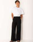Person wearing a white top and black wide leg pants on a white background